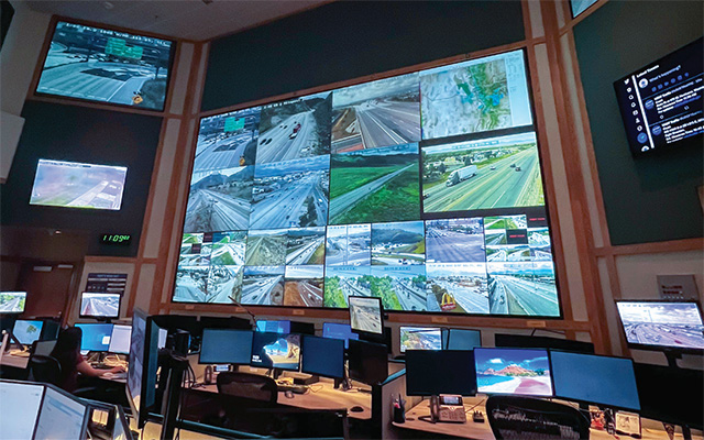 multiple desk and wall mounted visual displays in a control room show images of roads.